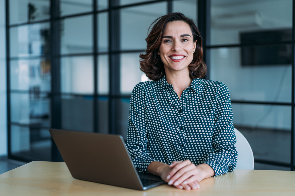 Portrait of elegant businesswoman sitting in her office looking at camera while using laptop.